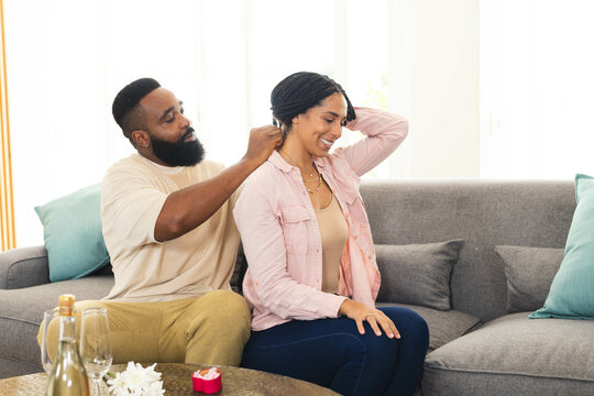 Man giving woman necklace gift at home, both smiling and enjoying moment