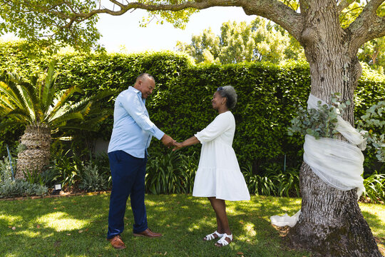 At wedding, Senior couple holding hands under tree in garden, enjoying sunny day together