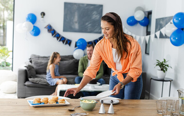 Woman preparing birthday party table while family enjoys time on couch