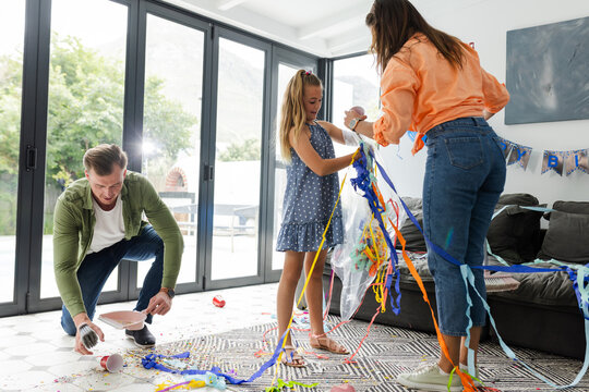 Family cleaning up colorful party streamers at home, enjoying teamwork together - Powered by Adobe