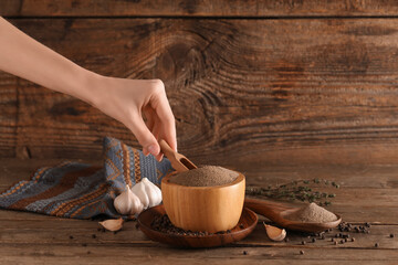 Female hand with scoop and bowl of black pepper powder on wooden background