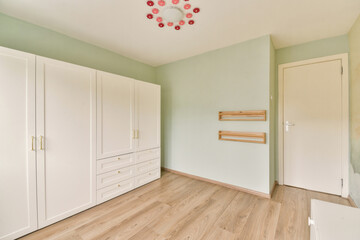 A spacious room featuring light green walls, wooden flooring, and minimalist storage solutions, creating a serene and contemporary living space.