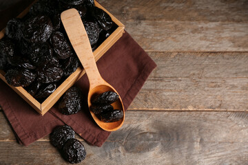 Box and spoon with dried prunes on wooden background