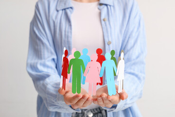 Woman holding colorful paper human figures on light background. Diversity and inclusion concept