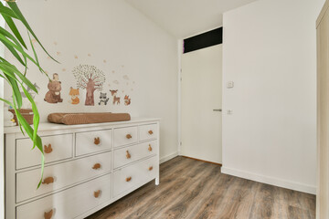A bright and inviting hallway featuring a stylish dresser, nature-inspired wall art, and wooden flooring, creating a warm atmosphere in the space.