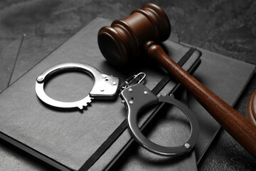 Handcuffs with judge's gavel and notebooks on dark background, closeup