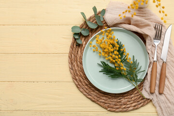Beautiful table setting with mimosa flowers and eucalyptus on yellow wooden background
