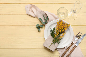 Beautiful table setting with mimosa flowers and eucalyptus on yellow wooden background