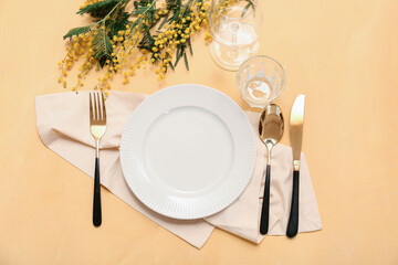Beautiful table setting with golden cutlery and mimosa flowers on yellow background
