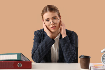 Young businesswoman suffering from loud noise at table on beige background