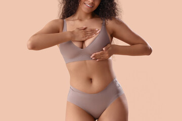 Naklejka premium Young African-American woman in underwear checking her breast on beige background. Cancer awareness concept