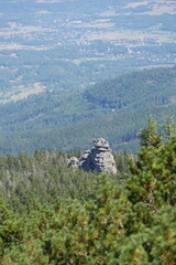 Rocky outcrop known as Three Rocks stands amidst a dense forest, overlooking a hazy valley and distant town under a bright sky