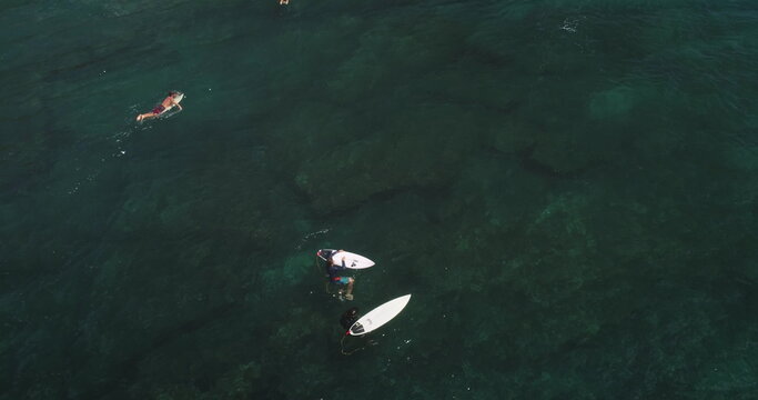 Aerial view of surfers waiting for waves in the ocean at Dreamland Beach, Bali, Indonesia, showcasing the beautiful turquoise waters and the anticipation of catching the perfect wave
