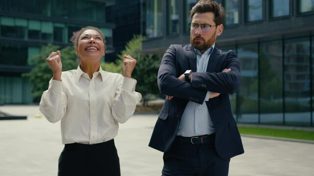 Happy successful smiling celebrating win African American woman businesswoman female in city joyful Caucasian man male businessman offended jealous envy different emotions two business colleagues