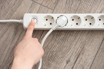 Female hand turning off extension cord on floor, top view. Unplug concept