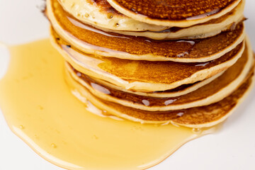 a tower of small milk pancakes on a ceramic bowl with natural yellow bee honey, close up