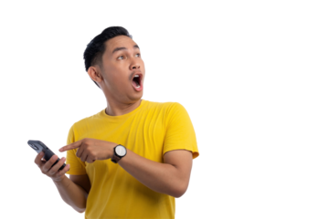 Surprised young Asian man holding smartphone and looking aside at copy space isolated on transparent background