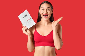 Happy young woman in underwear with menstrual calendar on red background