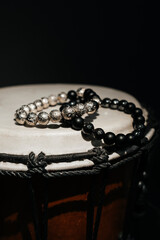 Black and silver beaded bracelets placed atop a traditional djembe drum. The beads' texture and the...