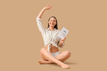 Young woman with menstrual calendar sitting on beige background
