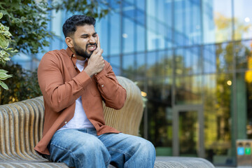 A man with a pained expression clutches his jaw, clearly suffering from a toothache while sitting...