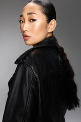 Fashion, asian woman, black leather jacket, ponytail hair an asian woman poses for the camera in a stylish black leather jacket with her hair pulled back in a ponytail