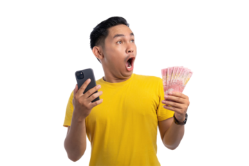 Excited handsome Asian man holding money and mobile phone, looking at copy space with shocked expression isolated on transparent background