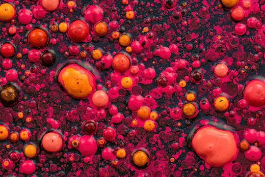 An abstract background of bobbly mixed pink, orange, and dark oil-based paints on a dark surface