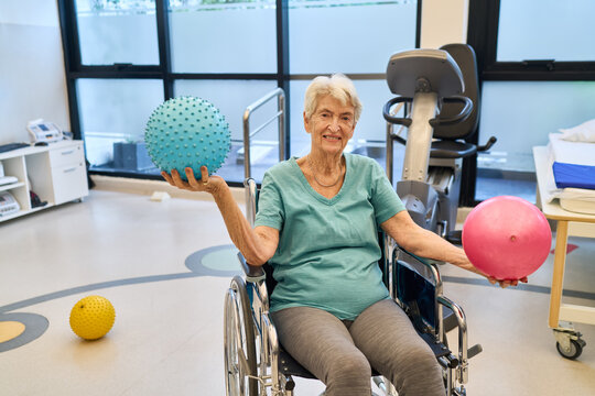 Senior woman in wheelchair exercising with balls in rehabilitation center