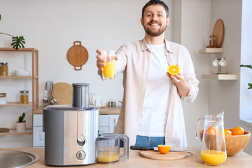 Young man with fresh orange juice and modern juicer in kitchen