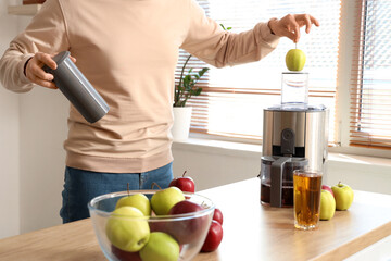 Young man making apple juice in kitchen