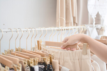 Hand Selecting Light Fashion Items from Wooden Hangers in Boutique