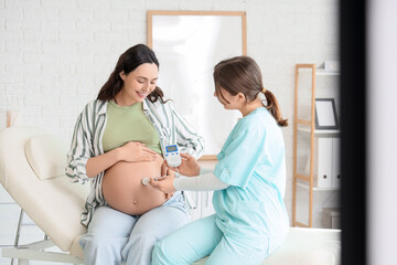 Female doctor with fetal doppler listening to baby's heartbeat in clinic