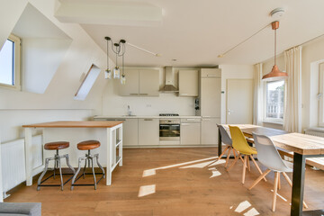 A bright and airy modern kitchen featuring sleek cabinetry, a wooden dining table, and stylish bar...