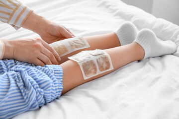 Mother applying mustard plasters on her ill daughter's legs in bedroom, closeup