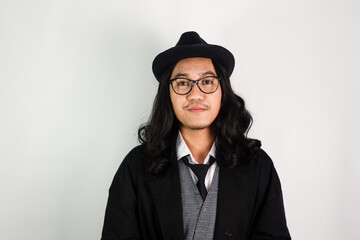 Asian man with long hair dressed as a mafia wearing glasses and a hat with a calm expression