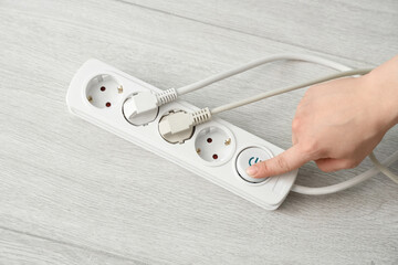 Female hand turning off extension cord with plugs on floor, top view