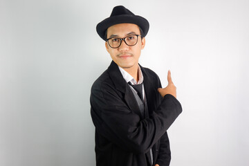 Asian man wearing a mafia-like suit and wearing glasses and a hat, with a smiling face, making a...