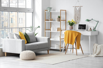 Interior of office with workplace, spring flowers in vase and sofa