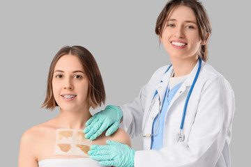 Female doctor applying mustard plaster on patient's chest against grey background