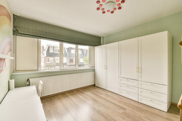 Bright and airy modern bedroom featuring a large window, minimalist white furniture, and soft green walls, creating a tranquil and inviting atmosphere.