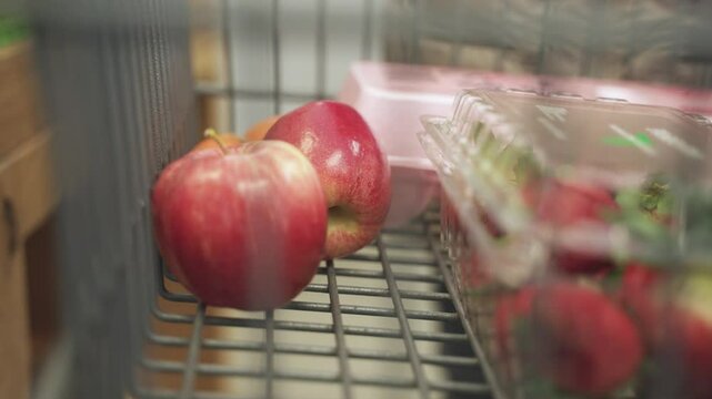 Apples getting kept by an unknow person in cart in a grocery store.