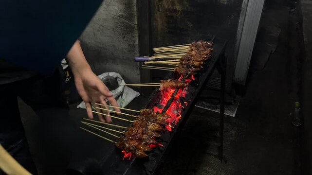 Southeast asian man grilling traditional madura chicken and mutton satay, on a street side stall in Indonesia, at the night