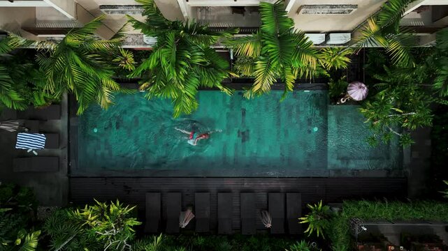 Aerial view of Active man,  swimming in pool, drone view from above, Bali villa, tropical vacation, holiday on island hotel resort