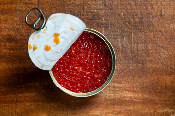 Opened metal tin can with red caviar on a wooden table, closeup, top view. Salmon cavia