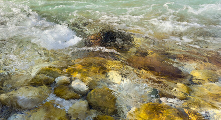 crystal clear transparent mountain river water flowing over assorted colorful golden stones. dynamic abstract nature pattern, shimmering light reflections, natural