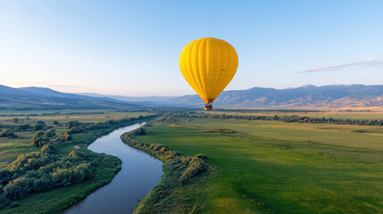 Obraz premium vibrant yellow hot air balloon floats gracefully over serene river, surrounded by lush green