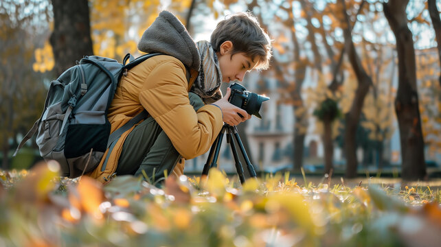 This Young photographer crouches on grass, focused on capturing vibrant autumn leaves in the park.