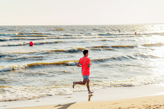 Sunlight Warms a Beach Runner on the Shore as Waves Dance Under a Clear Sky During Late Afternoon