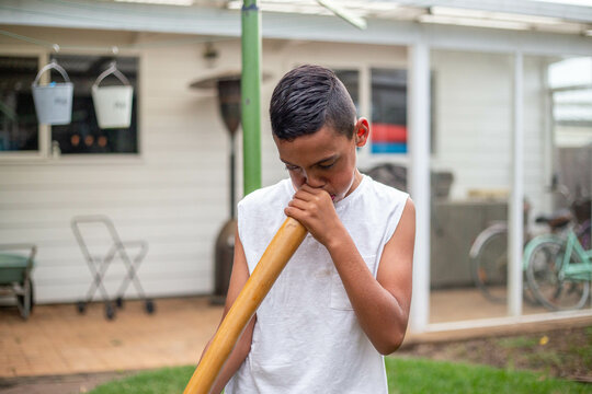 a boy in a white shirt blowing on a didgeridoo